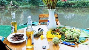 A table with a bottle of beer, a plate of food, a vase with flowers, and a plate of guava. - An Riverside Ecolodge (Tay Hoa Lu)