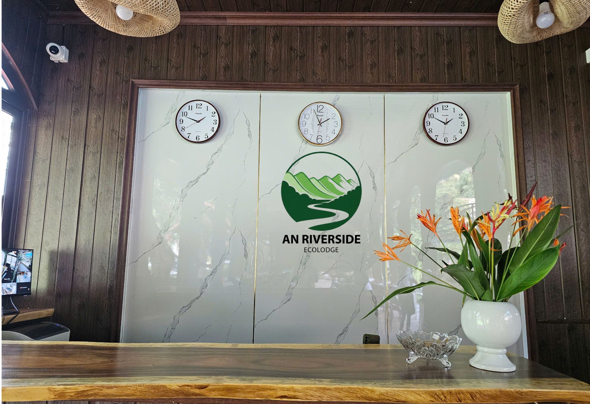 A reception desk with three clocks, a logo for An Riverside Ecododge, and a vase with flowers.