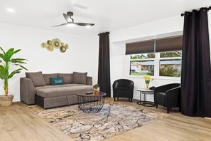 A modern living room with a sofa, a coffee table, a potted plant, and a view of the outside through a window.
