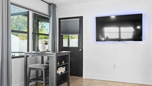 A room with a TV mounted on the wall, a door, and a window with curtains. - Venice Oasis | Pool, 3 King Beds, 2.5 miles >Beach (Venice)