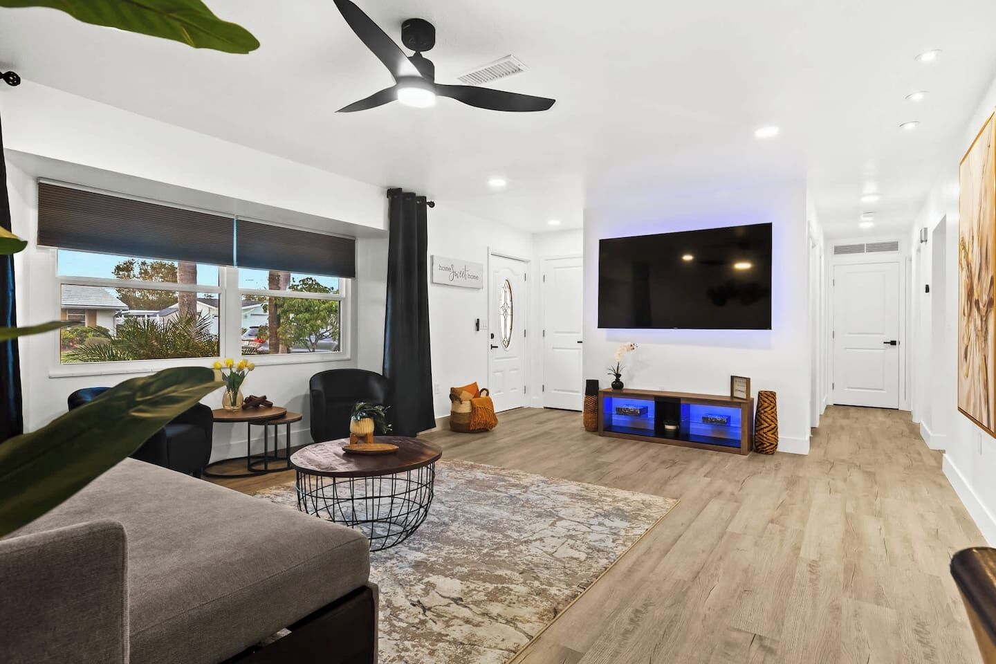 Ein modernes Wohnzimmer mit großem Fernseher, Deckenventilator und Blick ins Freie.