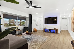 A modern living room with a large TV, ceiling fan, and a view of the outdoors. - Venice Oasis | Pool, 3 King Beds, 2.5 miles >Beach (Venice)