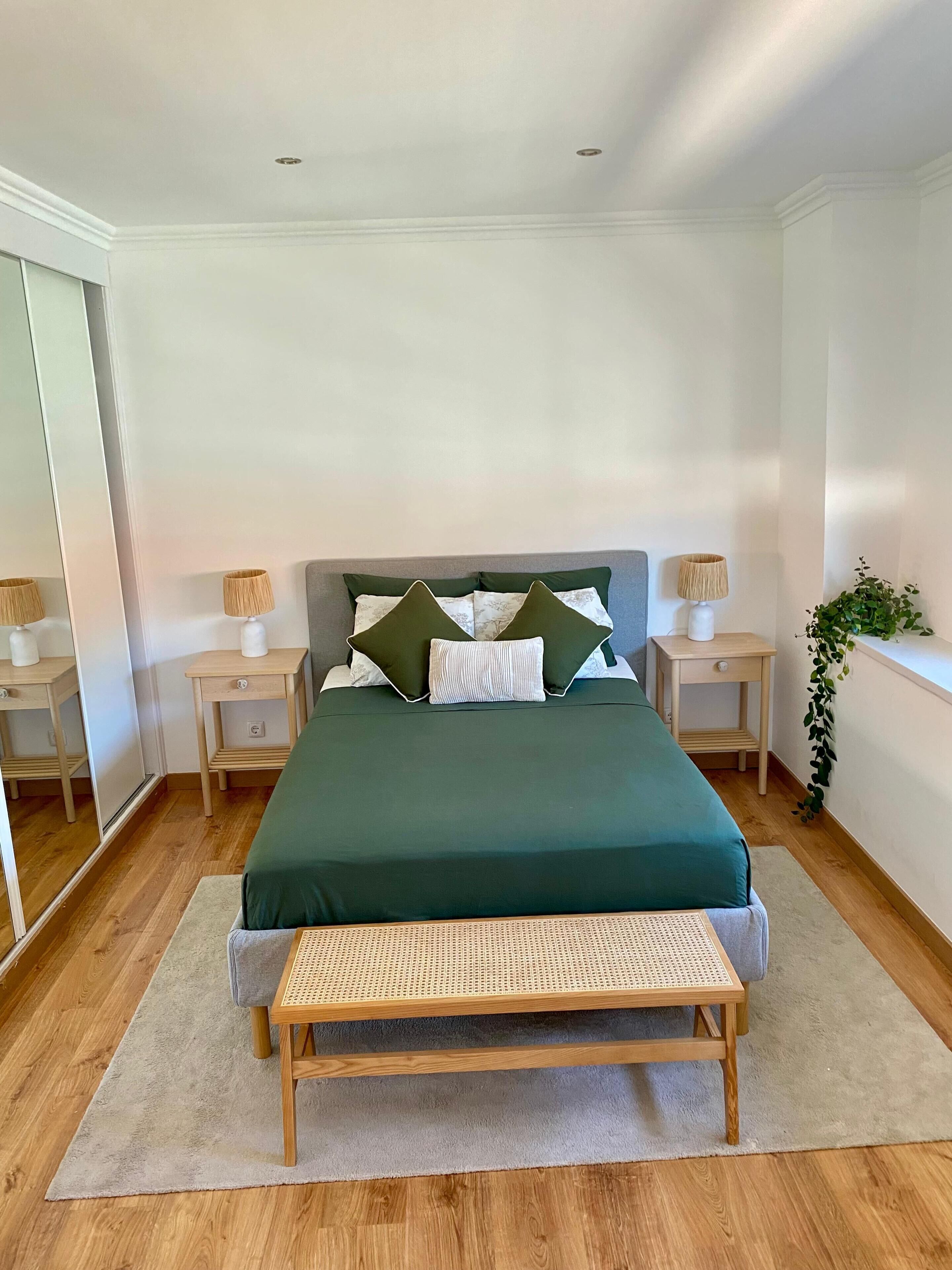 A neatly arranged bedroom with a bed, bedside tables, a bench, and a potted plant.