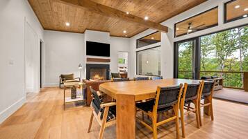 Un comedor moderno con una mesa y sillas de madera, una chimenea y ventanas amplias con vistas al exterior.