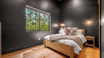 Ein Schlafzimmer mit großem Fenster, einem Bett mit Kissen, einem Nachttisch aus Holz und einem Cowhide-Teppich.