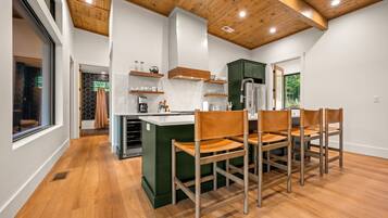 Una cocina moderna con vigas de madera en el techo, una isla central con sillas y vistas al exterior.