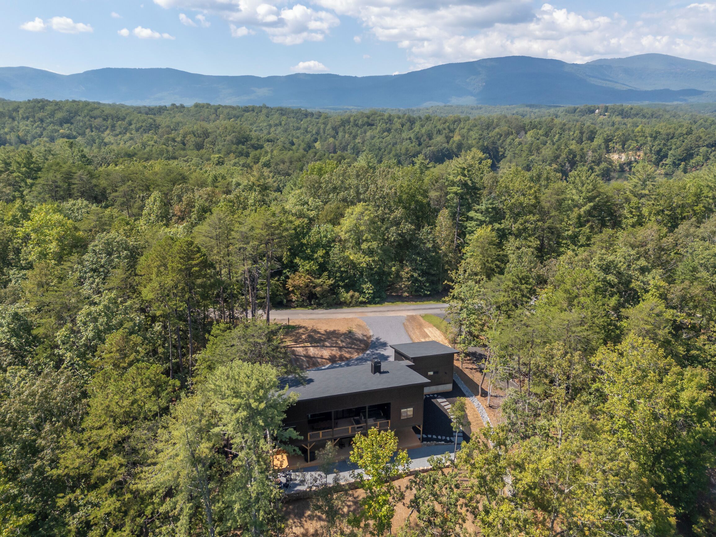 Una casa moderna rodeada de un bosque frondoso y con una vista despejada de montañas lejanas.