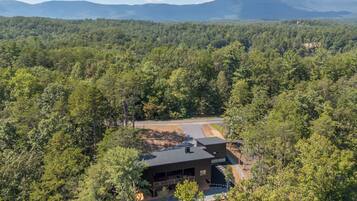 Una casa moderna rodeada de un bosque frondoso y con una vista despejada de montañas lejanas.