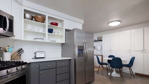 A modern kitchen with a built-in microwave, stainless steel refrigerator, and a gas stove. There is a dining area with a white table and blue chairs. - 10min to Downtown Bend Chic 2bdr (Bend)