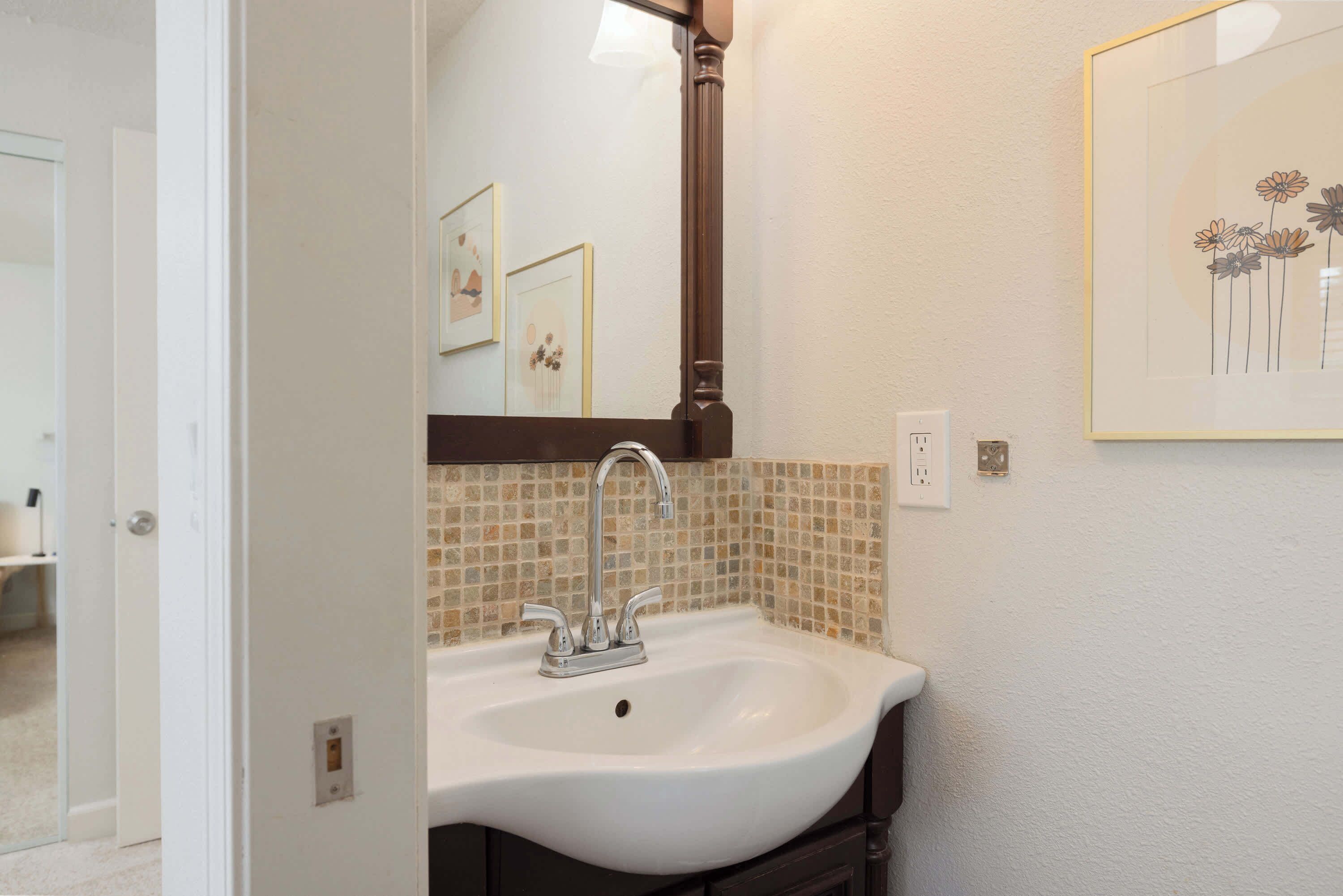 A bathroom with a white sink, a mirror, and a tiled backsplash.