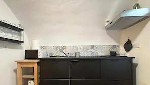 A compact kitchen with a black countertop, a wooden side table, and a patterned backsplash. - Palazzo Lomellini Historic Retreat (Genova)