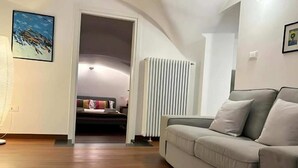 A modern living room with a beige sofa, wooden flooring, a radiator, and a door leading to a bedroom. - Palazzo Lomellini Historic Retreat (Genova)
