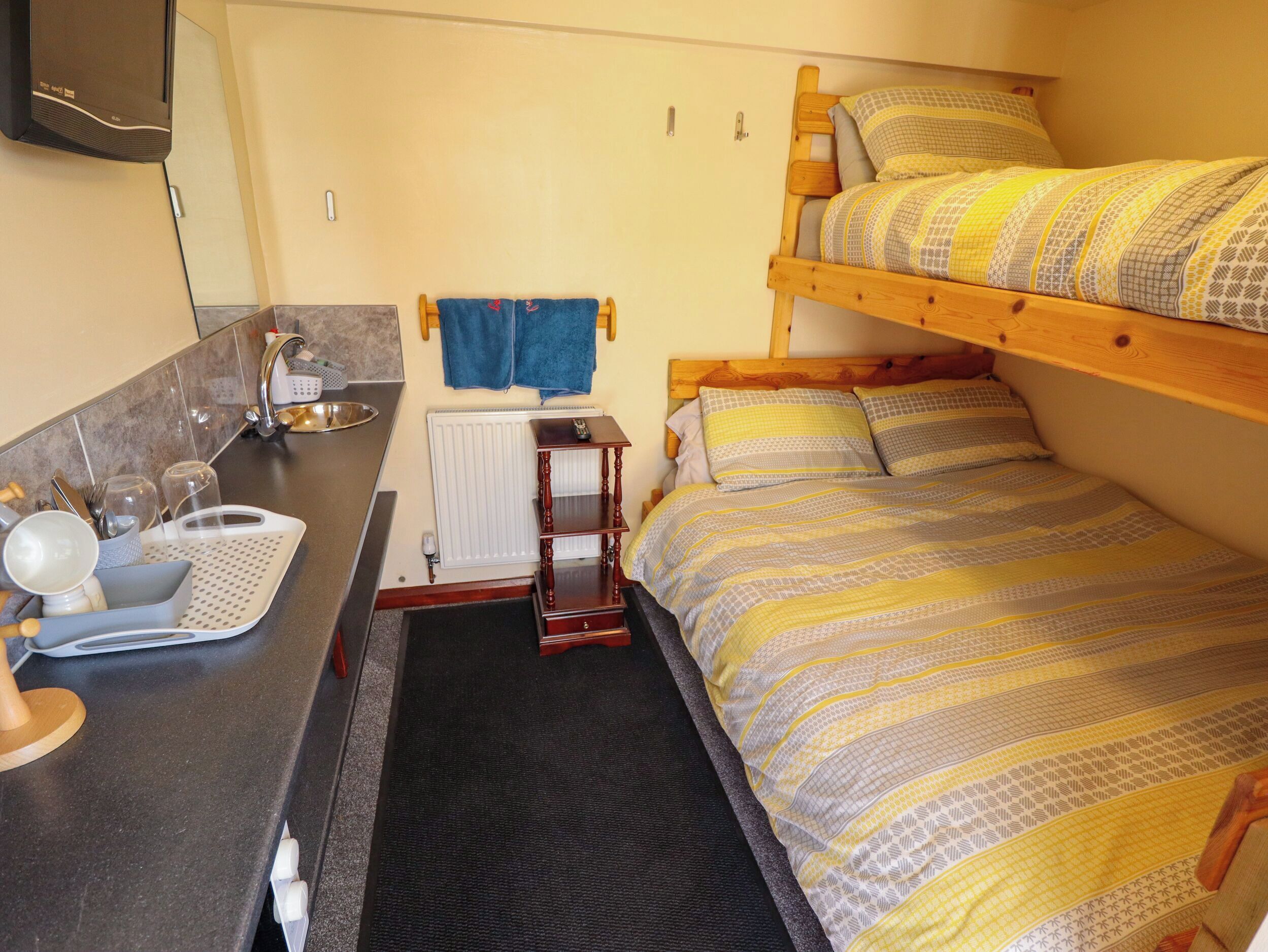 Une petite chambre comprenant un lit superposé, un coin cuisine, un évier et un miroir.