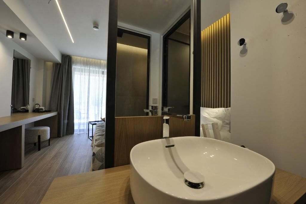 A modern hotel bathroom with a large white sink, a mirror, and a wooden vanity.