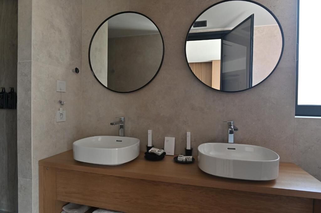 Un baño moderno con dos espejos redondos, un mueble de tocador de madera y un lavabo blanco.