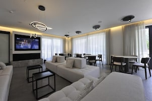 Una habitación de hotel moderna con un televisor de pantalla plana grande, un sofá, una mesa de comedor con sillas y una cama grande.