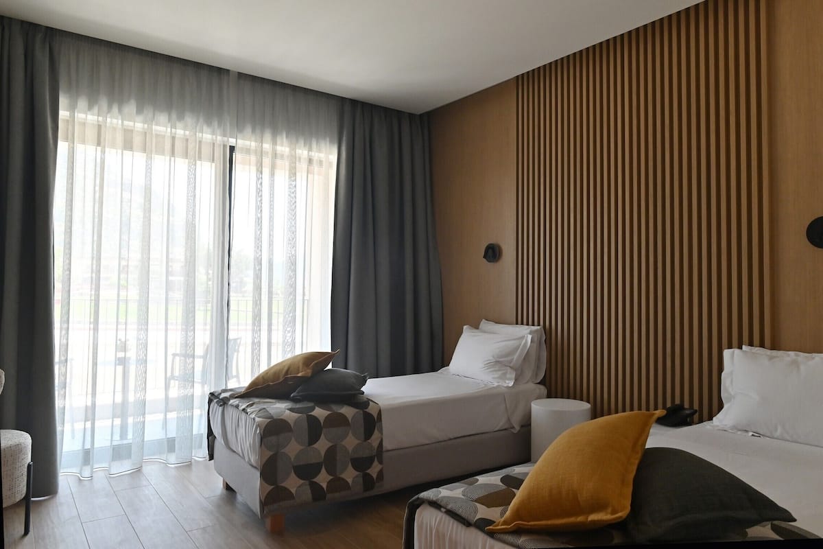 Habitación de hotel con dos camas, un sofá, una mesita y una ventana con cortinas.
