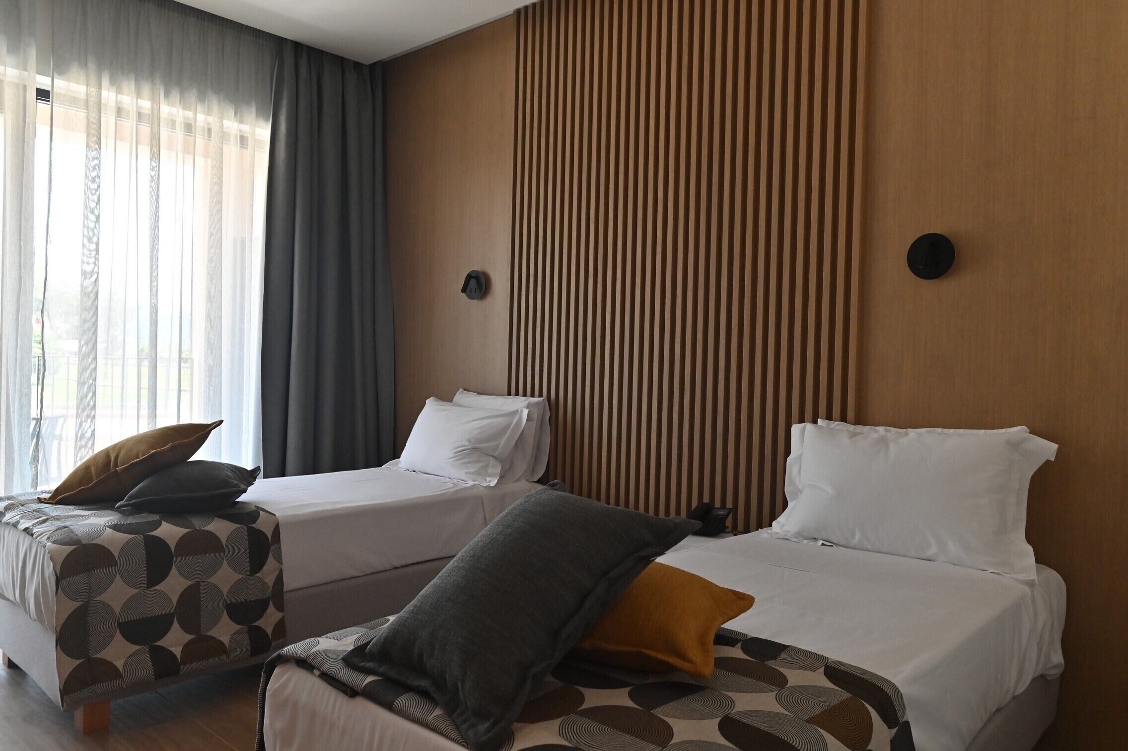 Quarto de hotel com duas camas, uma janela grande com cortinas e um painel de parede de madeira.