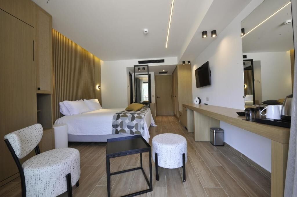 Une chambre d’hôtel moderne équipée d’un lit, d’un bureau, d’une chaise, d’une petite table, d’une poubelle et d’un téléviseur fixé au mur.