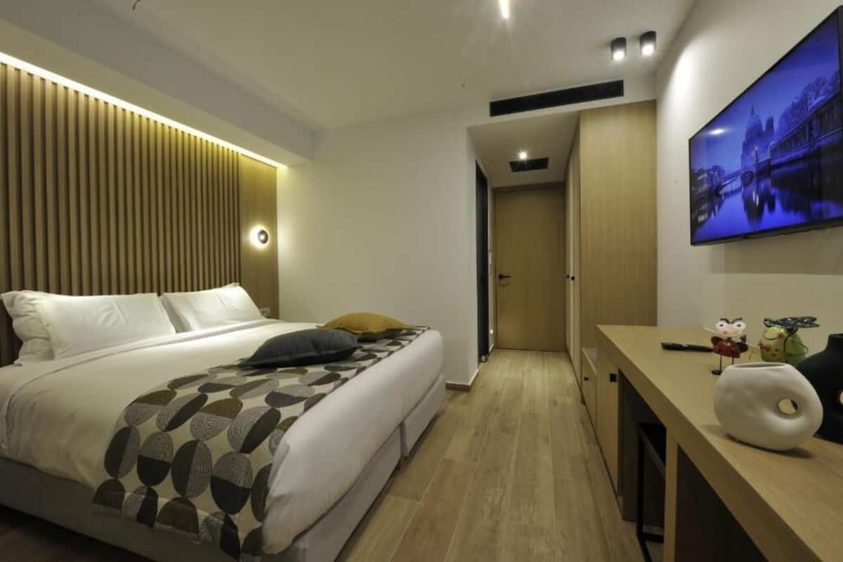 Una habitación de hotel moderna con cama, escritorio, televisor y un panel de pared de madera.