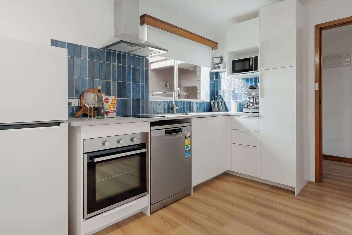 A modern kitchen with white cabinetry, a dishwasher, an oven, and a blue-tiled backsplash.