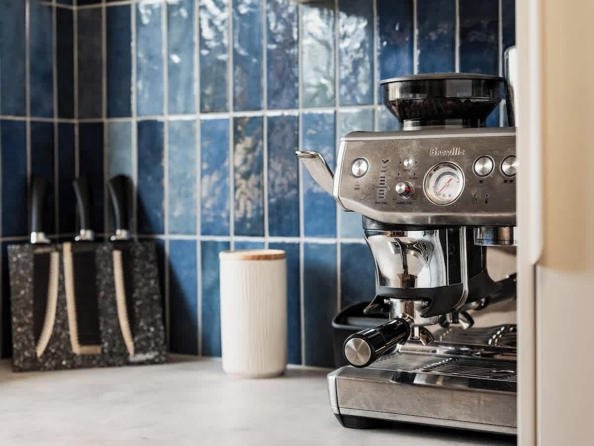 En kaffemaskin med en digital display och knappar, en vit pappersmugg och en svart väska med handtag.