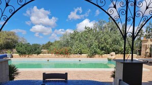 A poolside area with a tiled table, two chairs, and a decorative metal arch. - Riad Ahlam villa with swimming pool surrounded by argan trees (Essaouira)