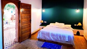 A bedroom with a bed, two bedside lamps, a wooden door, and a view of an outdoor area. - Riad Ahlam villa with swimming pool surrounded by argan trees (Essaouira)