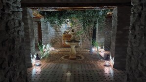 A stone-walled corridor with a tiled floor, a central fountain, and potted plants. - Riad Ahlam villa with swimming pool surrounded by argan trees (Essaouira)
