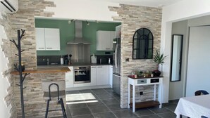 A modern kitchen with stone walls, a central island, and a dining area with a table. - Villa Ghjuvan (Peri)
