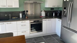 A modern kitchen with white cabinets, stainless steel appliances, and a grey tiled floor. - Villa Ghjuvan (Peri)