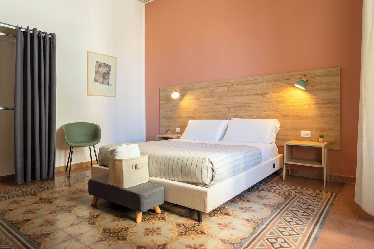 Un dormitorio con una cama, una silla verde, una mesita y una mesilla de noche.