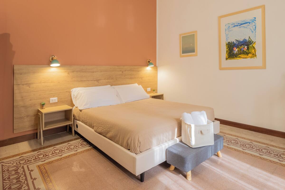 Una cama bien hecha con cabecera, mesitas de noche y una pequeña lámpara de noche.