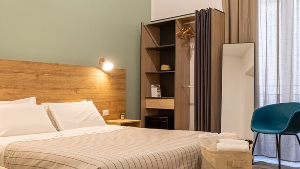 A neatly arranged hotel room with a bed, bedside table, wardrobe, and a chair. - EXPA  (Palermo)