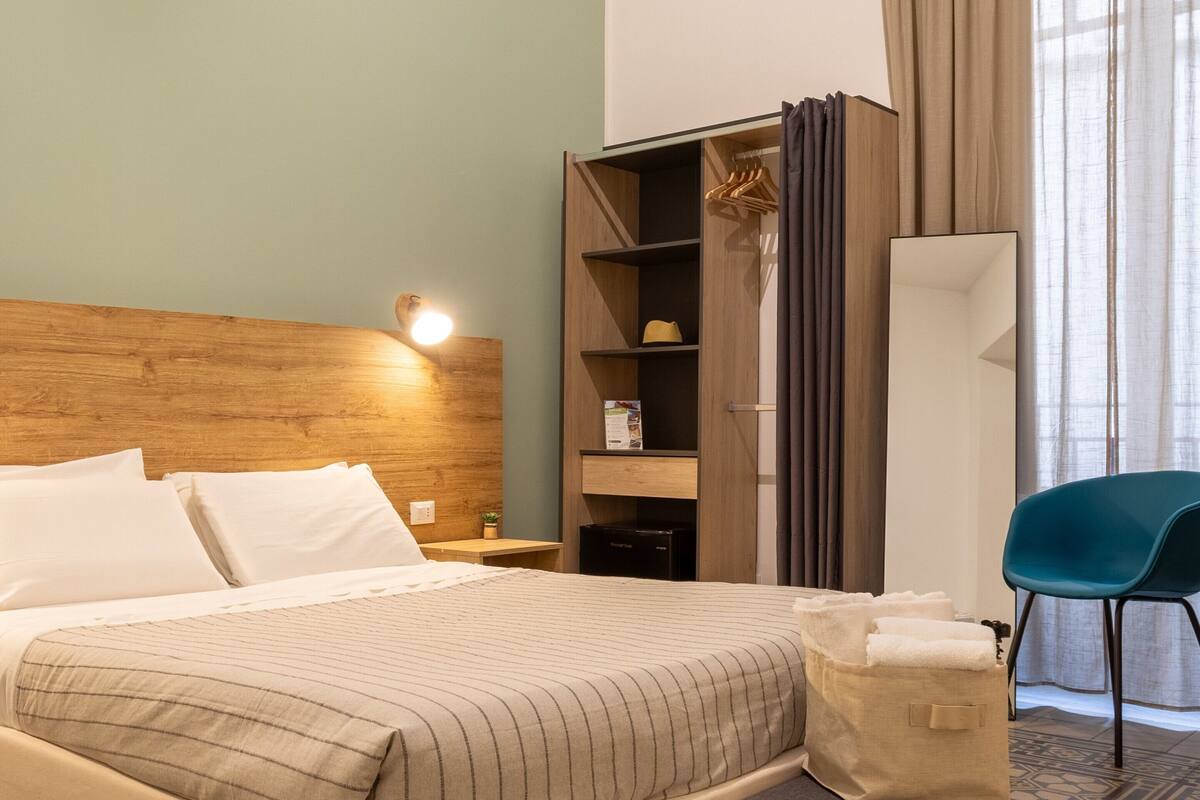 Una habitación de hotel ordenada con cama, mesita de noche, armario y una silla.