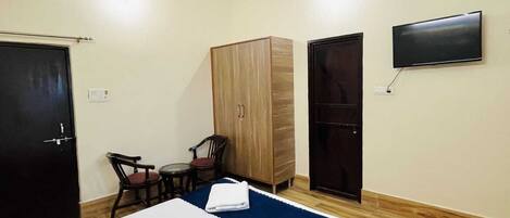 A hotel room with a bed, a desk, two chairs, a wardrobe, and a TV on the wall.
