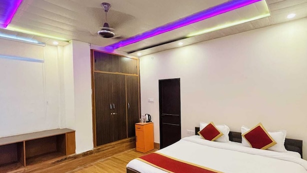 Un dormitorio moderno con suelo de madera, una cama grande con ropa de cama blanca y roja, un armario, una mesita con una tetera y un ventilador de techo.