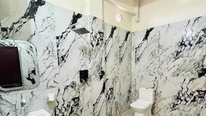 Un baño con pared de mármol, un lavamanos, un inodoro y un cubo de basura.