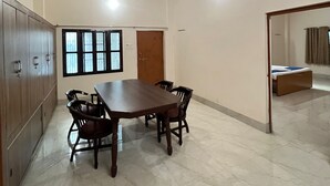 Una habitación con una gran mesa de madera y sillas, un ventilador de techo y una cama en la esquina.