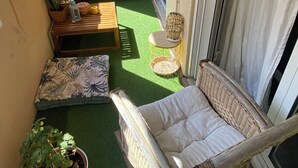 Un balcón con una silla de mimbre, una mesita pequeña, una planta en maceta y un sofá.