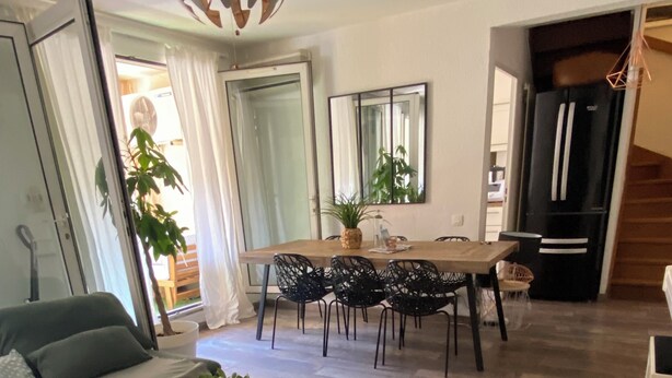 Una sala moderna con una mesa de centro de madera, un sofá y un comedor con mesa y sillas. Hay una planta sobre la mesa y un espejo grande en la pared.