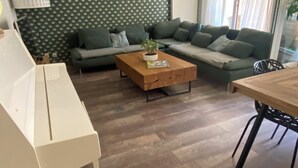 Una sala de estar moderna con una pared verde estampada, una mesa de centro de madera, un conjunto de sofás y una zona de comedor con una mesa y sillas.