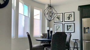 Un coin repas avec une table ronde, quatre chaises rembourrées, un lustre et des œuvres d’art encadrées accrochées au mur.