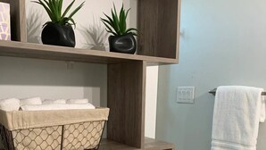 Une salle de bain avec des étagères en bois où sont rangées des serviettes et des plantes en pot.