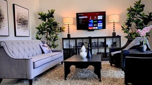 Un salon moderne avec un canapé gris, une table basse noire et un téléviseur fixé au mur, diffusant des services de streaming.