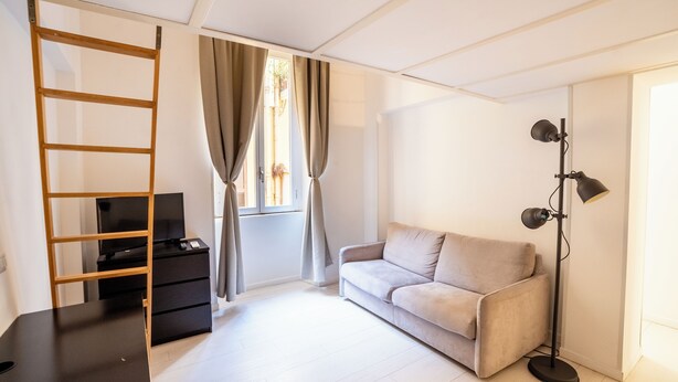A modern living room with a sofa, a TV on a stand, a floor lamp, and a window with curtains. - Rome City Center modern loft - special offer (Roma)