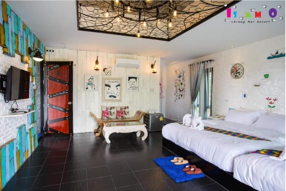 A hotel room with a bed, a small table, a TV, and a wall with artwork.