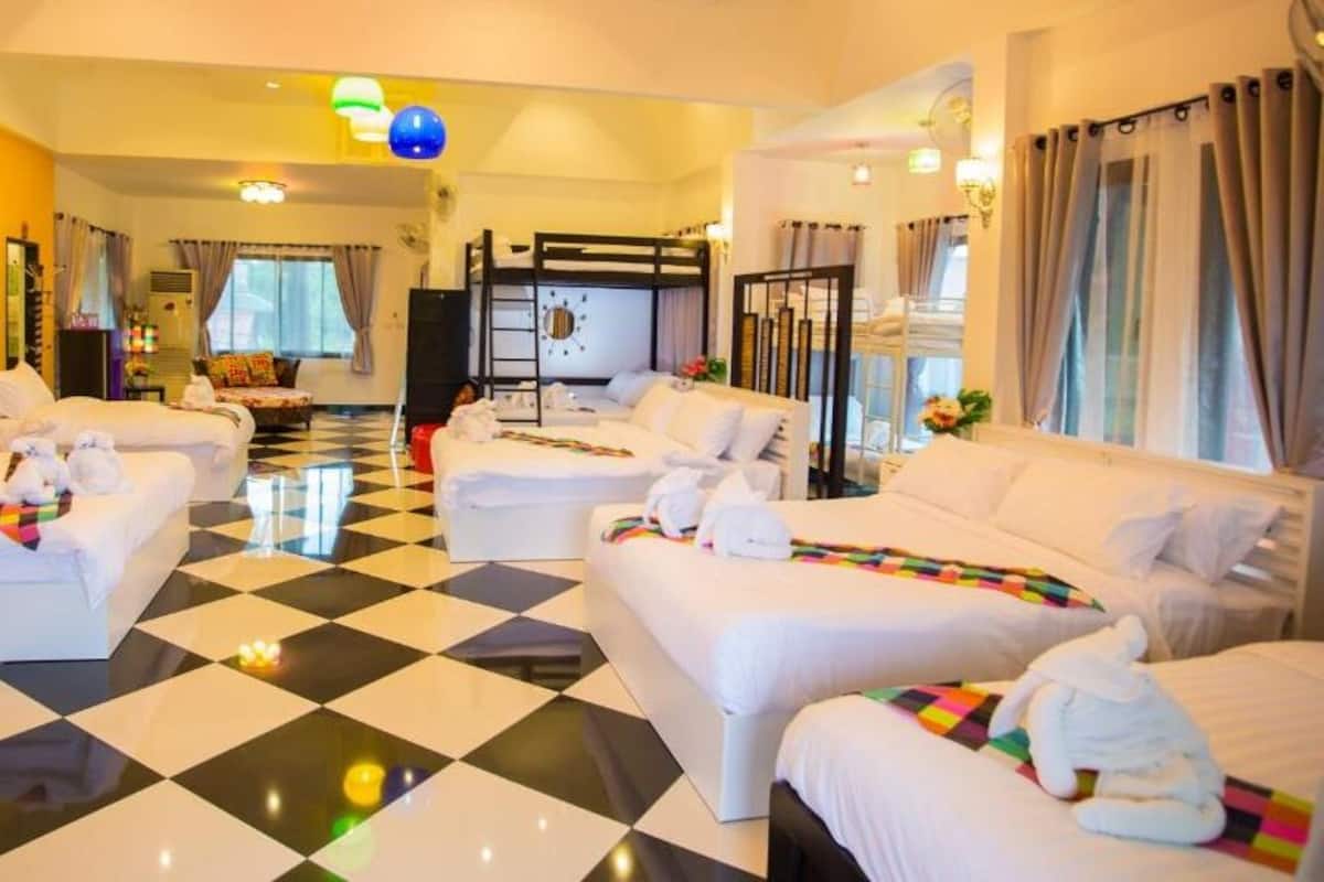 A hotel room with a checkered floor, multiple beds, a TV, and a balcony with curtains.