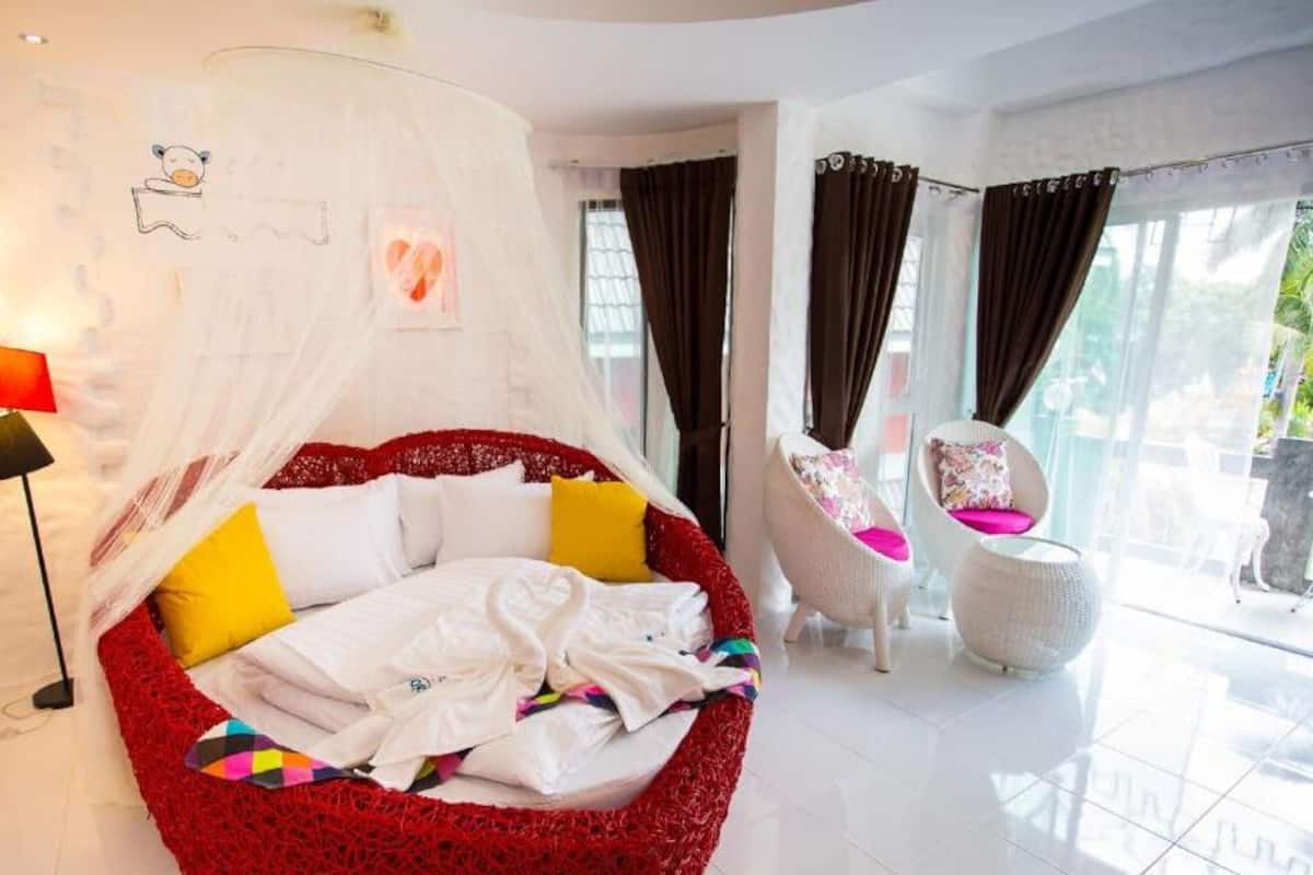 A bedroom with a red canopy bed, a white chair with a pink cushion, and a large window with curtains.