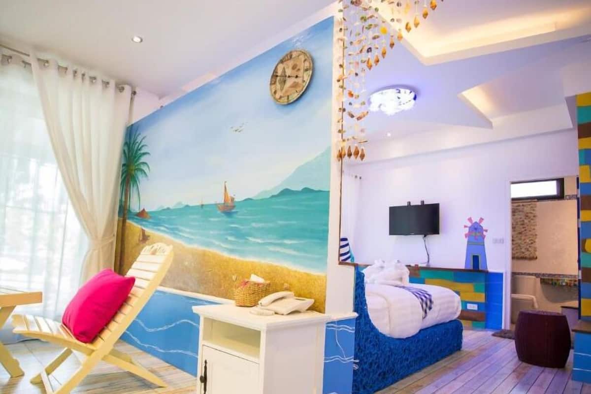 A beach-themed room with a mural, a bed, a TV, and a dining area.